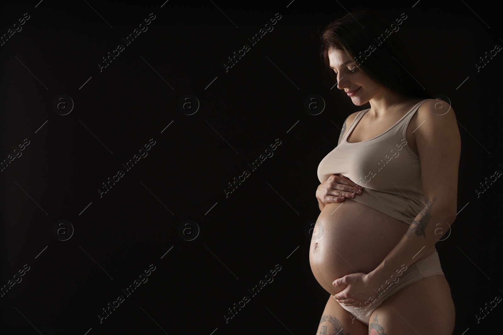 Photo of Beautiful pregnant woman with cute belly on black background. Space for text