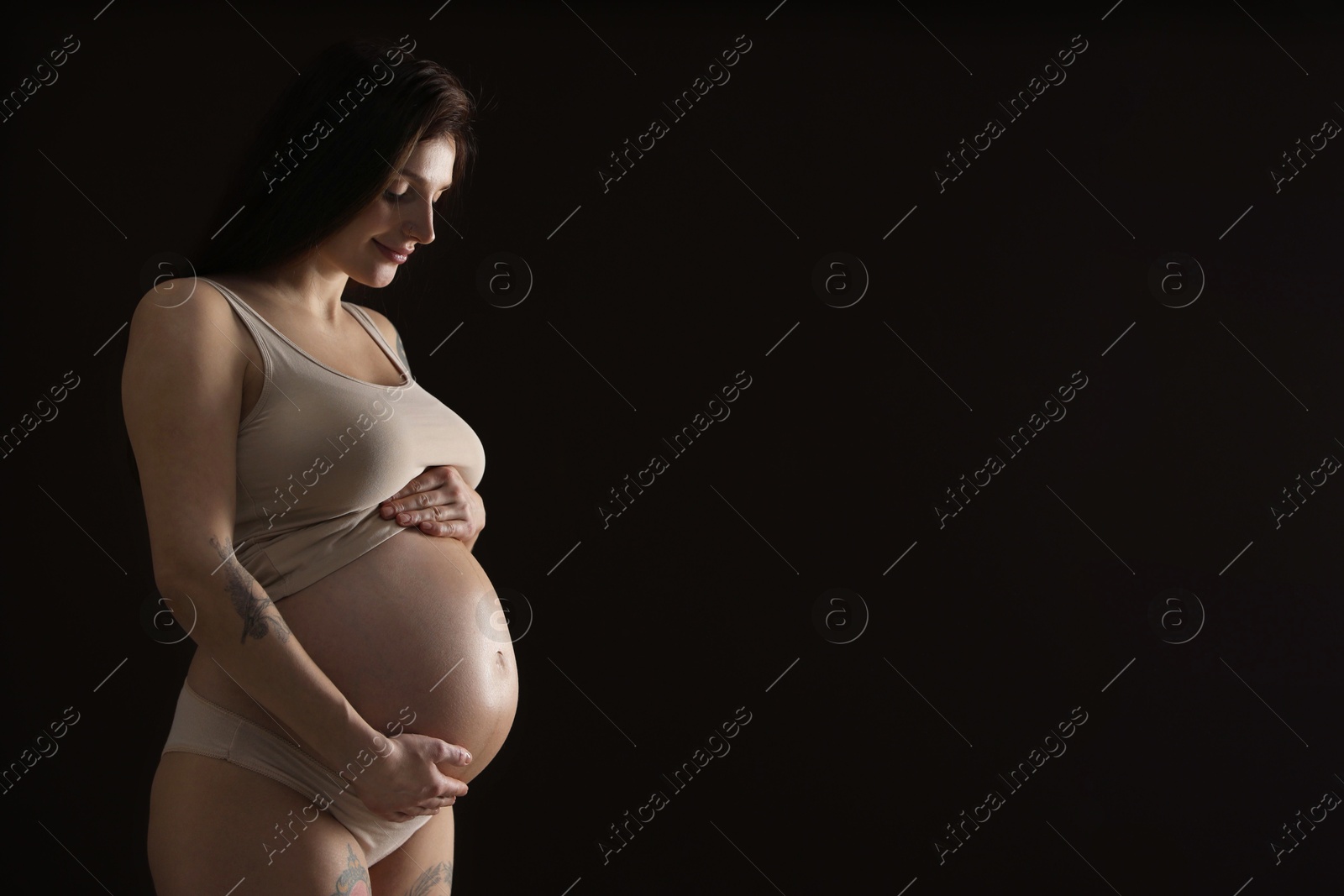 Photo of Beautiful pregnant woman with cute belly on black background. Space for text