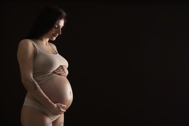 Photo of Beautiful pregnant woman with cute belly on black background. Space for text