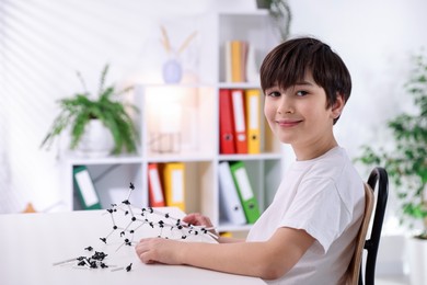 Photo of Boy making DNA structure model at desk indoors. Space for text