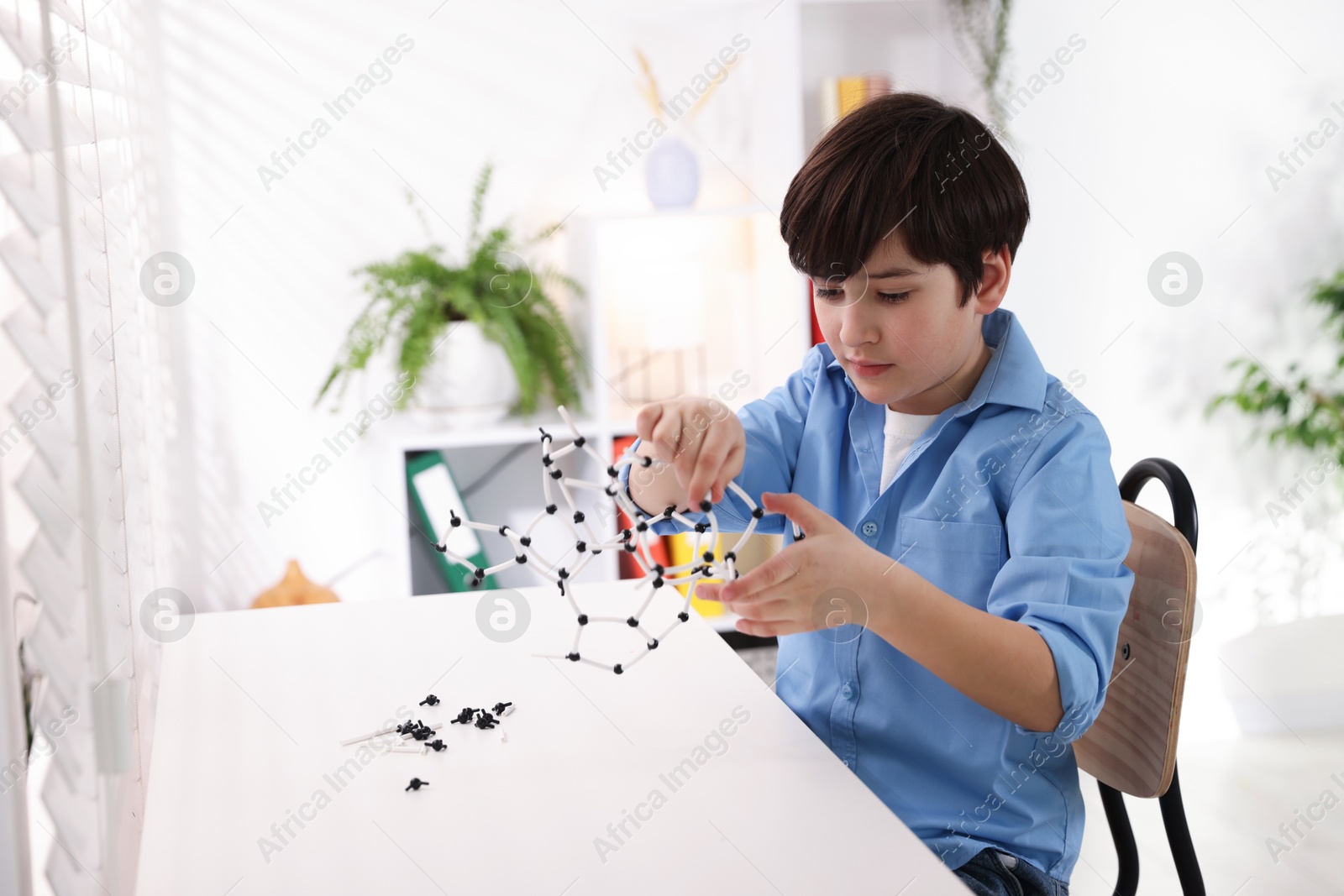 Photo of Boy making DNA structure model at desk indoors. Space for text