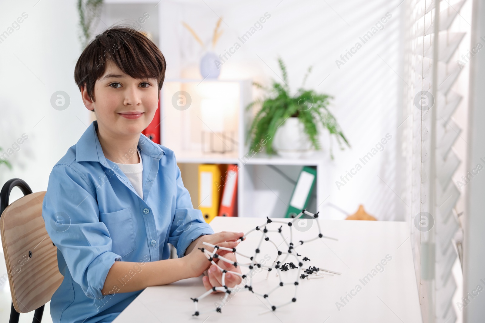 Photo of Boy making DNA structure model at desk indoors. Space for text