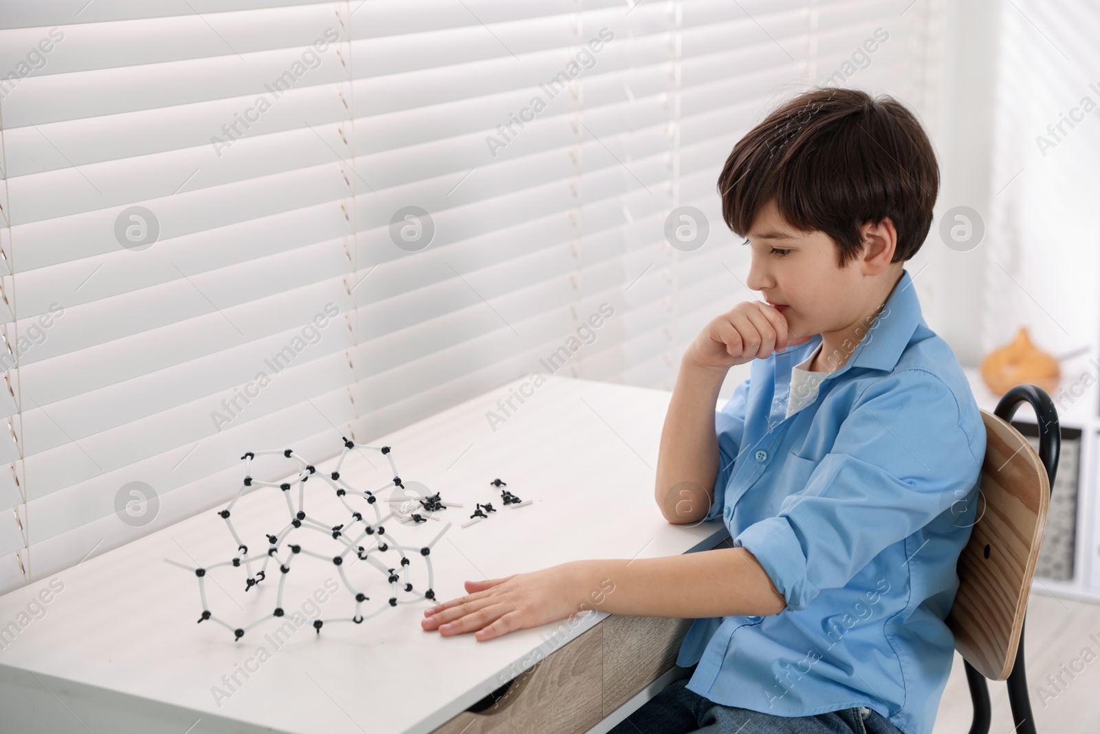 Photo of Boy making DNA structure model at desk indoors. Space for text