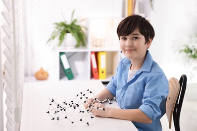 Photo of Boy making DNA structure model at desk indoors. Space for text