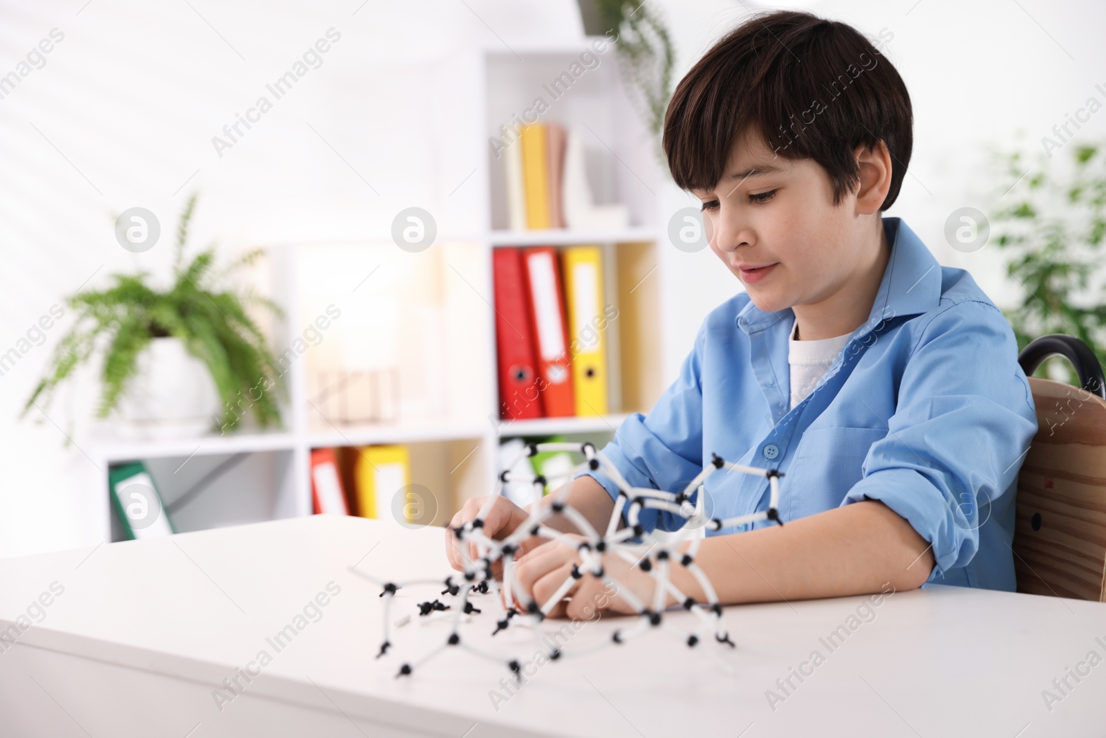 Photo of Boy making DNA structure model at desk indoors. Space for text