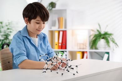 Photo of Boy making DNA structure model at desk indoors. Space for text