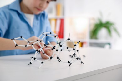 Photo of Boy making DNA structure model at desk indoors, closeup. Space for text