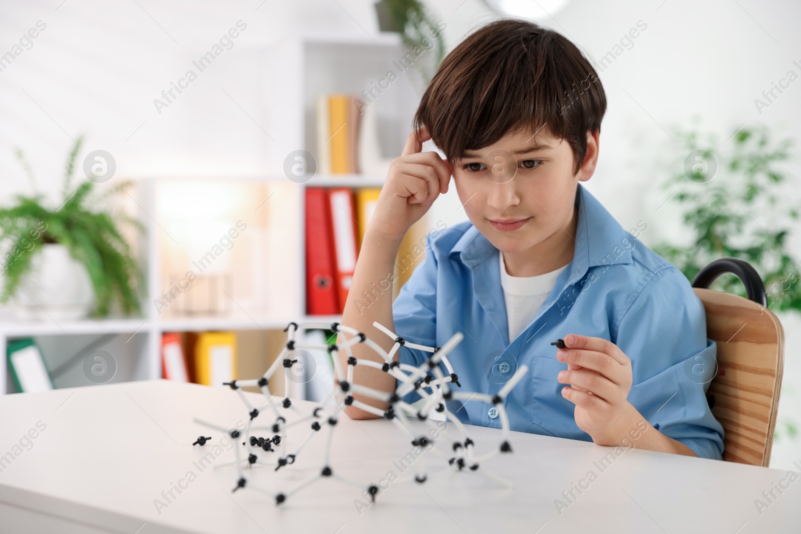 Photo of Boy making DNA structure model at desk indoors. Space for text