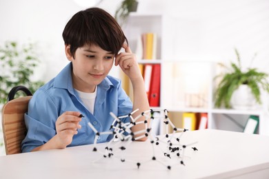 Photo of Boy making DNA structure model at desk indoors. Space for text