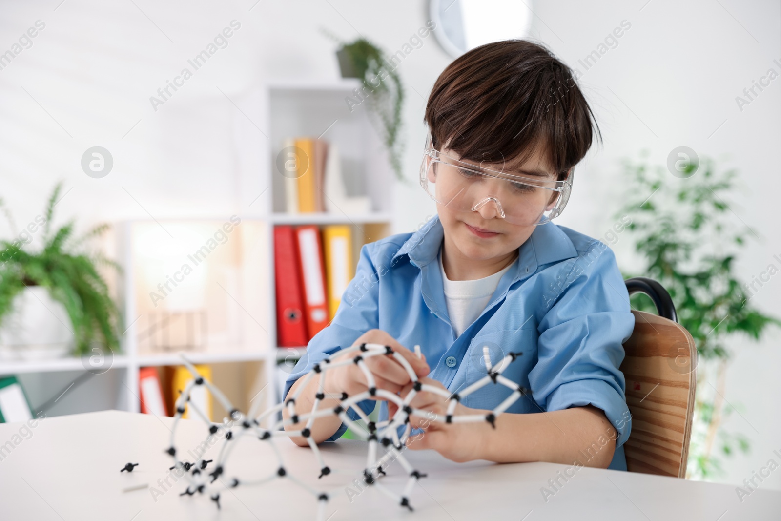 Photo of Boy making DNA structure model at desk indoors. Space for text