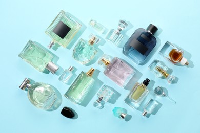 Photo of Bottles of various perfumes on light blue background, flat lay