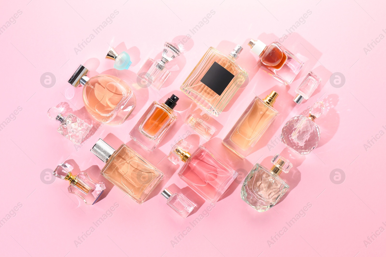 Bottles of various perfumes on pink background, flat lay Photo of Bottles of various perfumes on pink background, flat lay