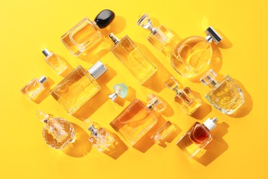 Photo of Bottles of various perfumes on yellow background, flat lay
