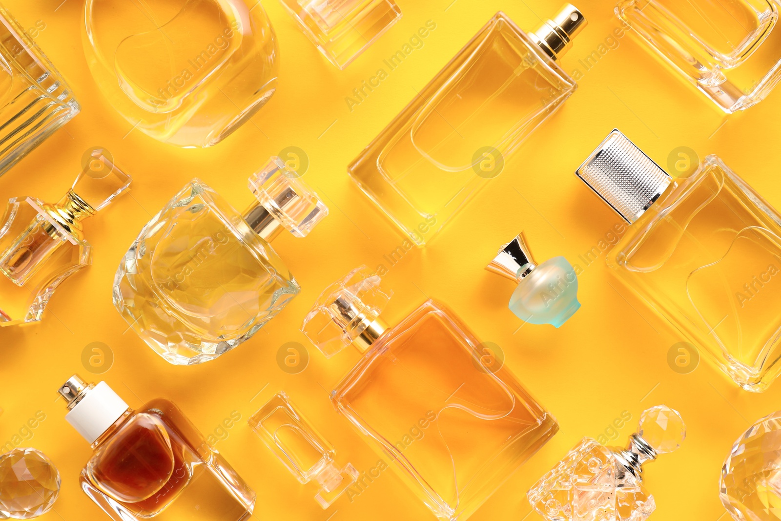 Bottles of various perfumes on yellow background, flat lay Photo of Bottles of various perfumes on yellow background, flat lay