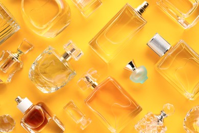 Photo of Bottles of various perfumes on yellow background, flat lay