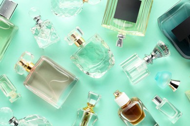 Photo of Bottles of various perfumes on turquoise background, flat lay