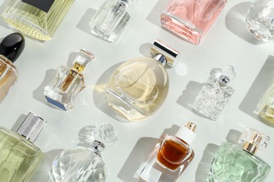 Photo of Bottles of various perfumes on light background, flat lay