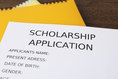 Photo of Scholarship application form and notebooks on wooden table, closeup