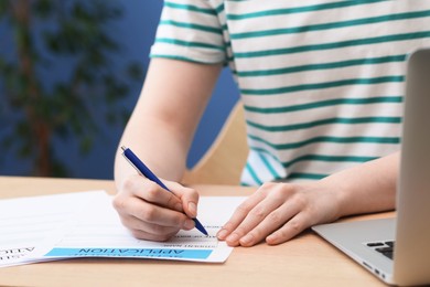 Photo of Student filling scholarship application form at wooden table, closeup