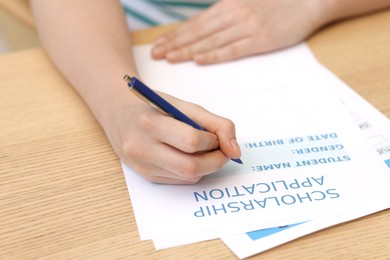 Photo of Student filling scholarship application form at wooden table, closeup