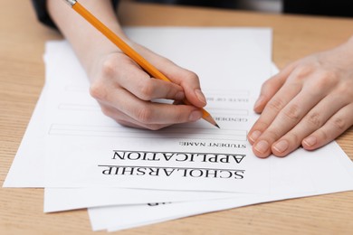 Photo of Student filling scholarship application form at wooden table, closeup