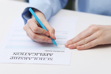 Photo of Student filling scholarship application form at white table, closeup