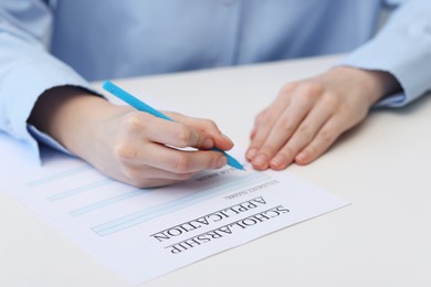 Photo of Student filling scholarship application form at white table, closeup