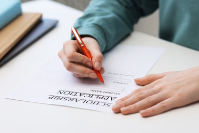 Photo of Student filling scholarship application form at white table, closeup