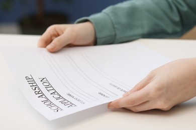 Photo of Student with scholarship application form at white table, closeup