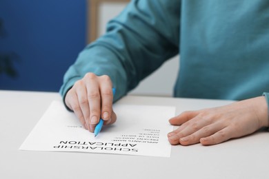 Photo of Student filling scholarship application form at white table, closeup