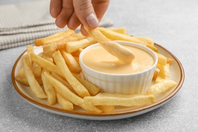 Photo of Woman dipping French fry into cheese sauce at grey table, closeup