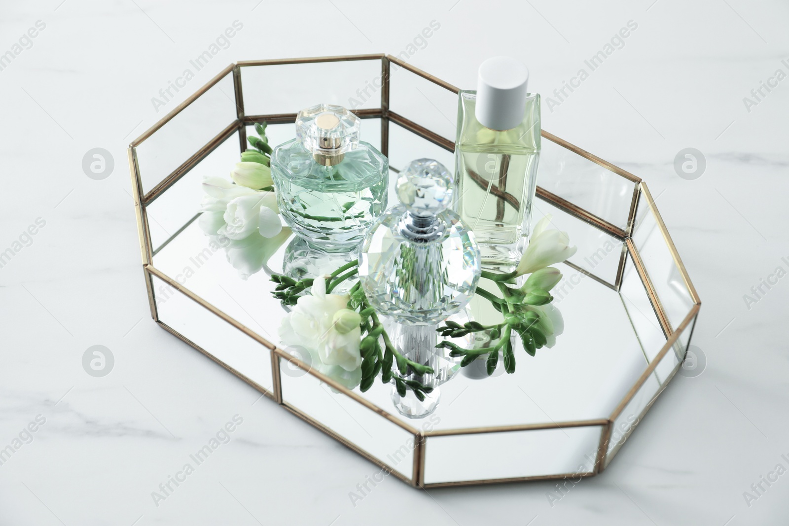 Tray with perfumes and beautiful flowers on white table Photo of Tray with perfumes and beautiful flowers on white table