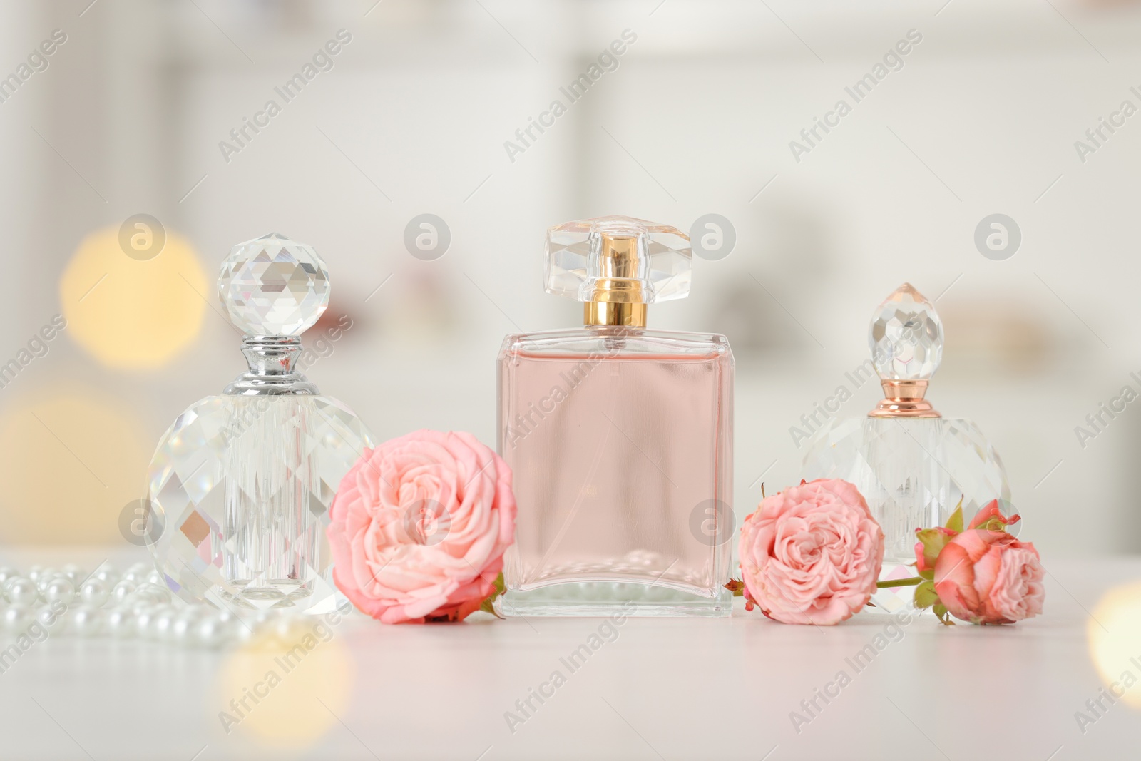 Bottles of perfume and beautiful flowers on white table Photo of Bottles of perfume and beautiful flowers on white table