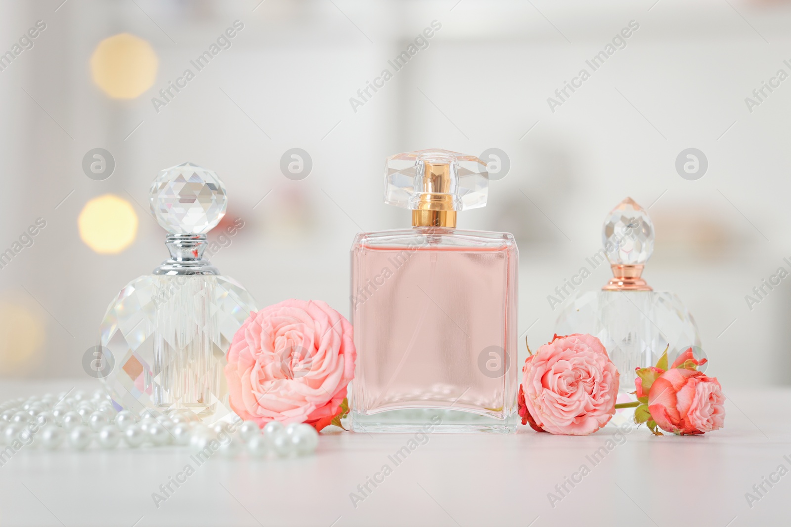 Bottles of perfume and beautiful flowers on white table Photo of Bottles of perfume and beautiful flowers on white table