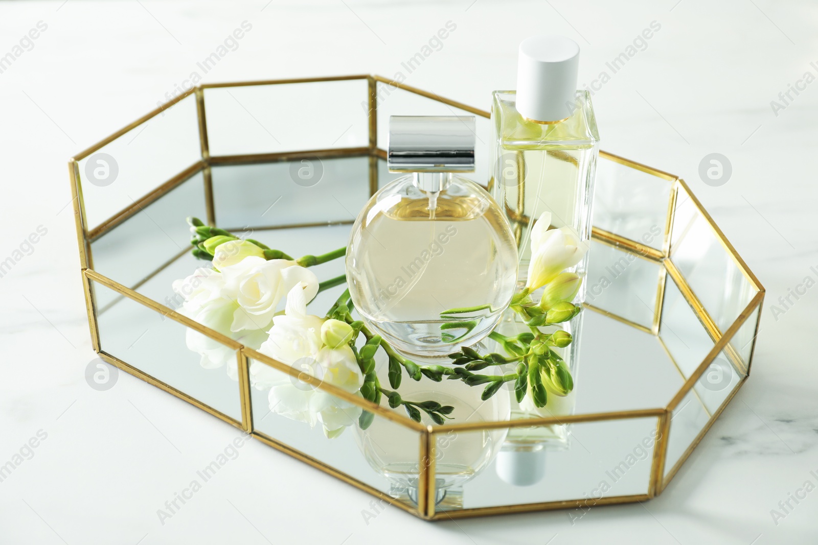 Tray with perfumes and beautiful flowers on white table, closeup Photo of Tray with perfumes and beautiful flowers on white table, closeup