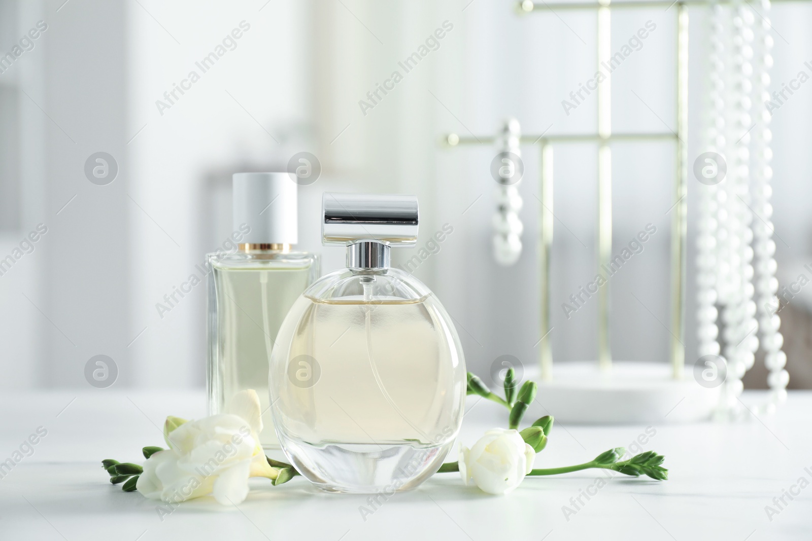 Bottles of perfume and beautiful flowers on white table Photo of Bottles of perfume and beautiful flowers on white table