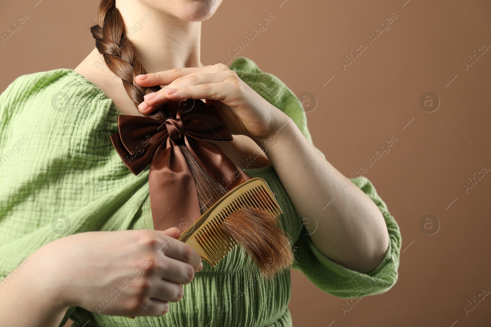 Photo of Woman with beautiful bow brushing her hair on brown background, closeup