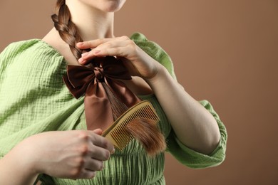 Photo of Woman with beautiful bow brushing her hair on brown background, closeup