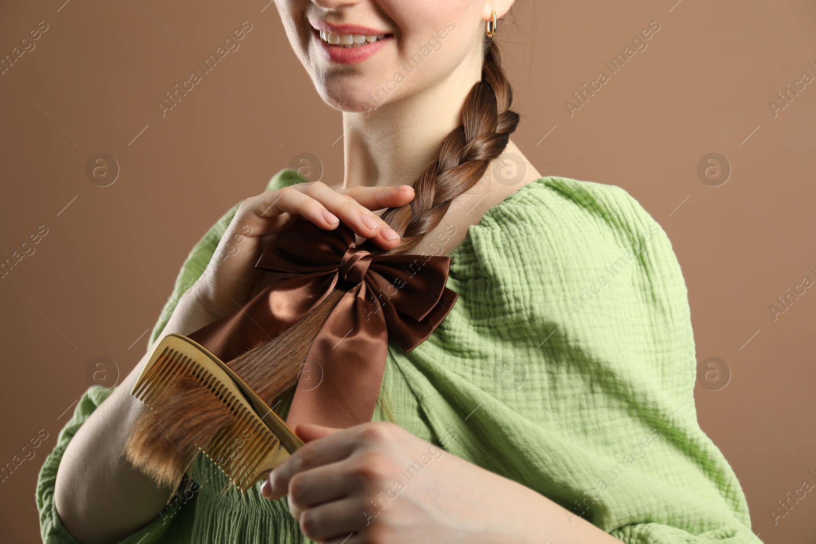 Photo of Woman with beautiful bow brushing her hair on brown background, closeup