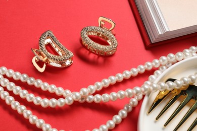 Photo of Different hair clips, pearl necklace and comb on red background, above view