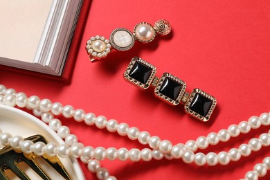 Photo of Different hair clips, pearl necklace and comb on red background, flat lay