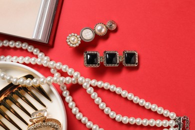 Photo of Different hair clips, pearl necklace and comb on red background, flat lay