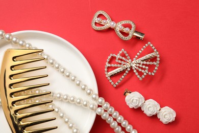 Photo of Different hair clips, pearl necklace and comb on red background, flat lay