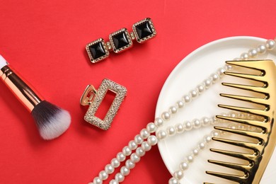 Photo of Different hair clips, pearl necklace, brush and comb on red background, flat lay