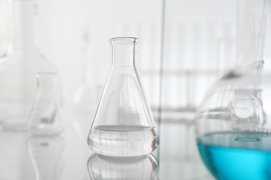 Photo of Flask with liquid on mirror surface against light background. Laboratory glassware