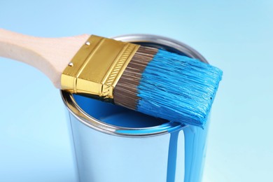 Photo of Can of blue paint and brush on light background, closeup