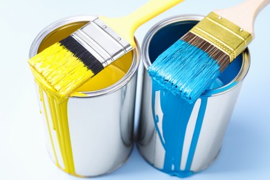 Photo of Cans of paint and brushes on light background, closeup