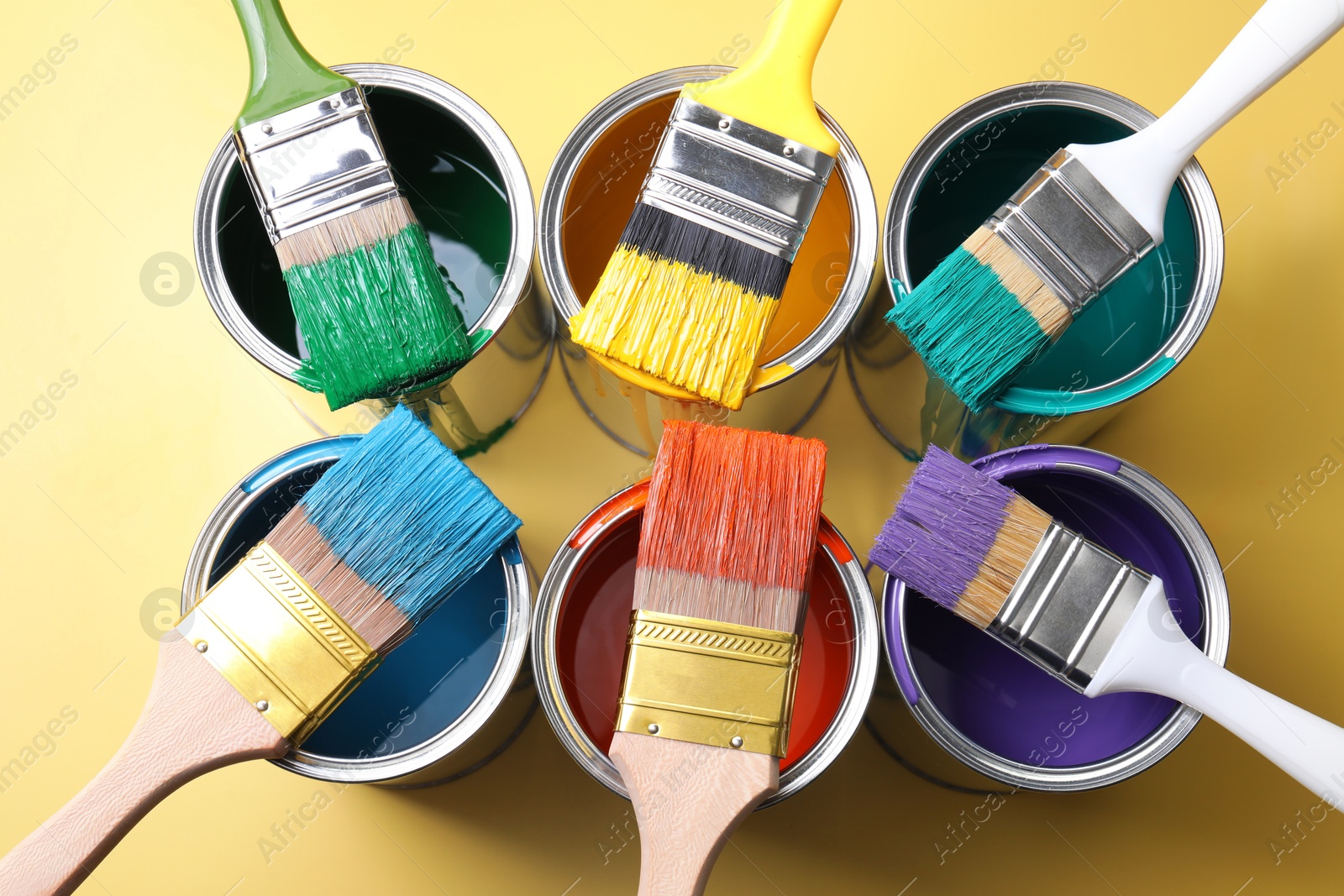 Photo of Cans of paint and brushes on yellow background, flat lay