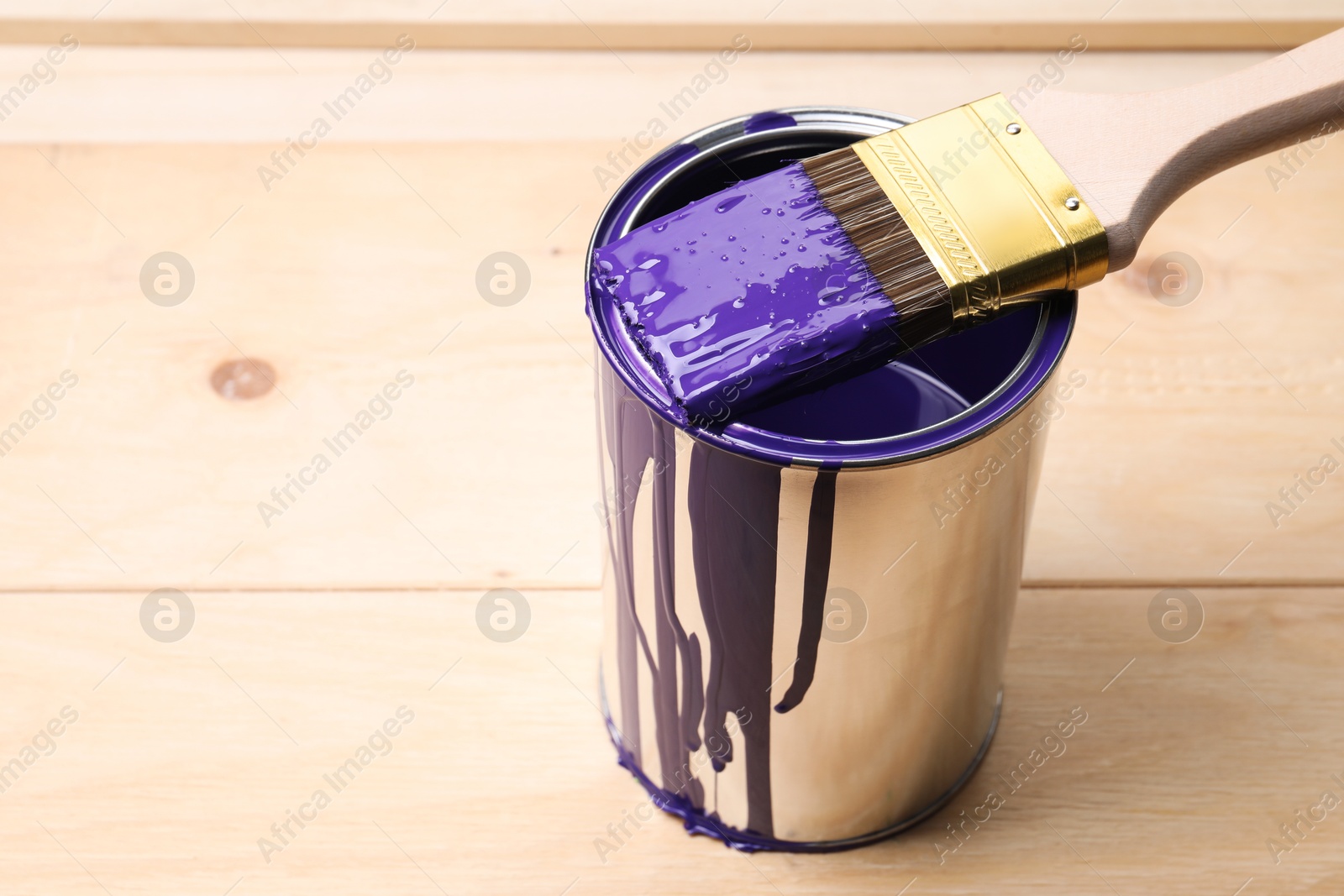 Photo of Can of purple paint and brush on wooden table, closeup. Space for text