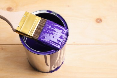 Photo of Can of purple paint and brush on wooden table, closeup. Space for text